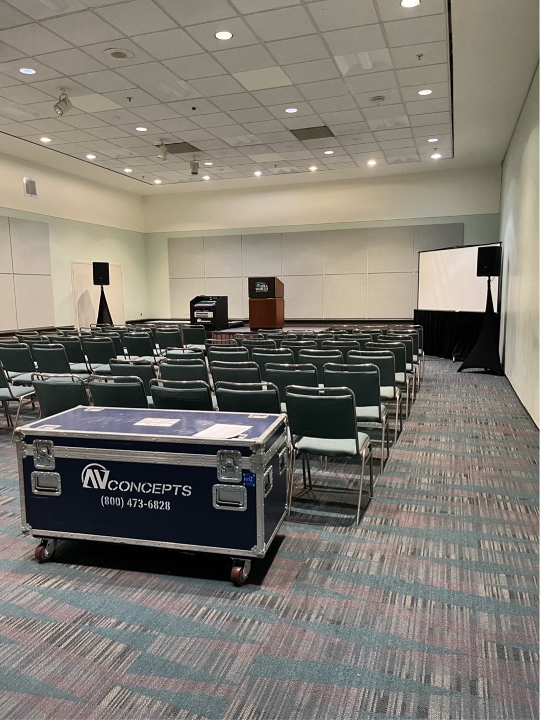 The inside of a room that will be used to host panels. There are rows of chairs on carpet and high ceilings.